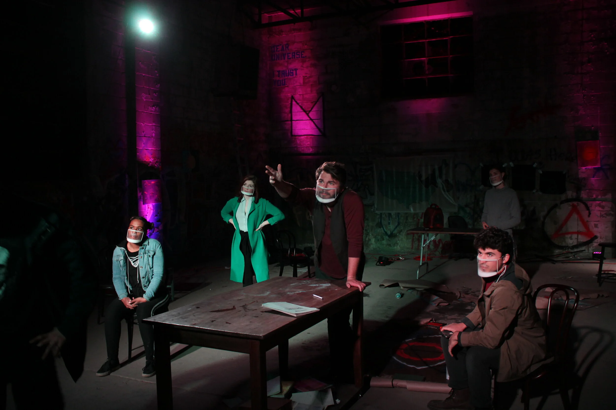 A scene from The Collective — performers in an immersive warehouse setting lit in magenta and teal